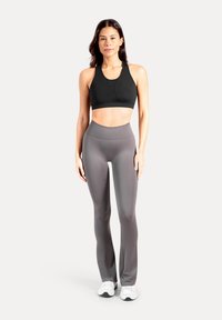 Zwarte atletische sportbeha met een afgeronde halslijn en racerback-ontwerp, gecombineerd met hoge, nauwsluitende grijze leggings. Witte sportschoenen.