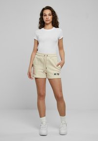 Vit kortärmad t-shirt i kombination med beige shorts med elastisk midja, som har sidofickor och en liten färgglad logotyp på vänster ben. Vita sneakers.