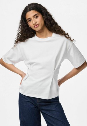 T-shirt en coton blanc à col rond et manches courtes, avec une coupe décontractée et des plis sur les côtés pour un peu de texture. Porté avec un jean bleu foncé.