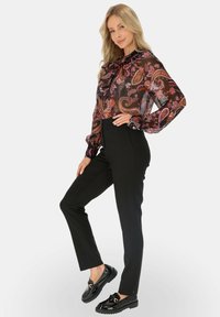 Przezroczysta czarna bluzka z wielokolorowym wzorem paisley, z wiązanym dekoltem, w połączeniu z dopasowanymi czarnymi spodniami i błyszczącymi czarnymi loafersami.