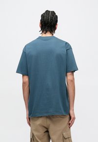 Camiseta de algodón azul con un corte holgado, mangas cortas y cuello redondo. Presenta una textura lisa sin patrones visibles.