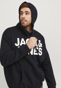 Schwarzer Kapuzenpullover mit Fronttasche, großer weißer Text "JACK & JONES", Kapuze mit Kordelzug und gerippten Bündchen. weicher Stoff, lockere Passform.