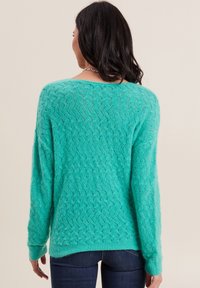 Türkiser Pullover mit strukturiertem, offener Strickmuster, langen Ärmeln und einem leicht geschwungenen Saum. Weicher, kuscheliger Stoff für zusätzliche Wärme.