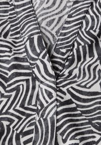 Tissu noir et blanc présentant un motif de zèbre ondulé avec des lignes courbes. Matière en coton avec une texture douce et des détails de couture visibles.