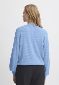 Hele sinine kudum särk tekstuurse chevron mustriga, langetatud õlavarred ja soonikkoes mansetid; kantud mustade pükstega.