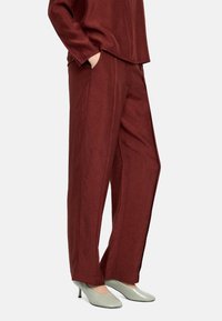 Bordowe, szerokie spodnie z teksturowanego materiału z bocznymi kieszeniami, w połączeniu z jasnozielonymi butami na wysokim obcasie.