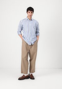 Camicia a righe blu e bianche con bottoni, pantaloni beige a gamba larga, mocassini marroni. Tessuto liscio, vestibilità comoda, maniche arrotolate, motivo discreto.