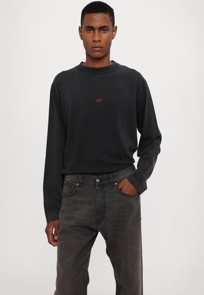 Crna majica dugih rukava s crvenim logotipom "424" na prsima, u kombinaciji sa sivim trapericama klasičnog kroja i prednjim džepovima.