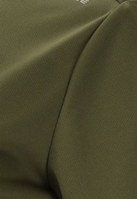 Close-up van olijfgroen textuurstof met kleine perforaties en een naaddetail.