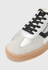 Sølv sneakers med overdel i semsket skinn og lær, svarte detaljer, teksturert grå såle og svarte lisser. Lett design med et moderne utseende.