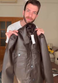 Hnedá kožená bunda s golierom, dvoma prednými vreckami a gombíkovými detailmi. Hladká štruktúra a viditeľné švy.