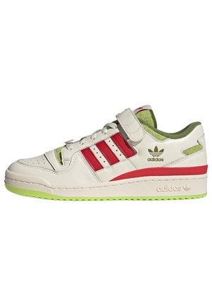Baskets basses Adidas blanches avec des rayures rouges, intérieur et semelle verts, laçage devant et une sangle velcro au-dessus des lacets.