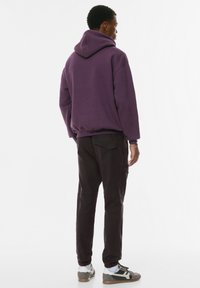 Lila hoodie med en avslappnad passform och känguruficka, kombinerad med mörka byxor och sneakers. Texturerat tyg, utan synliga mönster.