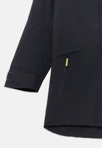 Casaco impermeável azul marinho com bainha reta, mangas longas, um bolso frontal com fecho e ajustadores de punho em Velcro. Textura de tecido suave e leve.