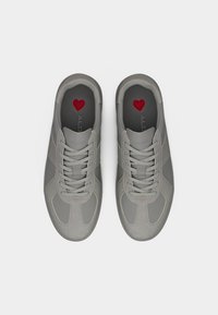 Paire de baskets grises à lacets avec des panneaux en daim et en tissu, vues de dessus, avec des formes de cœur rouges sur des semelles intérieures noires.