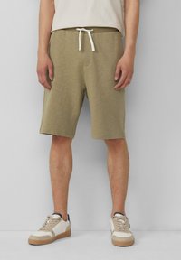 Khaki-Shorts aus weichem Stoff, mit einem elastischen Bund und einer weißen Kordel, sowie Seitentaschen. Dazu passende lässige Turnschuhe.