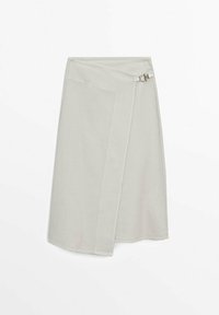 Jupe portefeuille beige clair avec rabat asymétrique à l'avant et petite boucle argentée sur fond blanc.