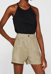 Žena v černém bezramínkovém halter topu zasunutém do béžových šortek s vysokým pasem, které mají knoflík a boční kapsy.