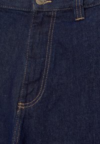 Denim w ciemnoniebieskim kolorze z widocznymi szwami. Ma przednią kieszeń i metalowe zapięcie na guzik. Tekstura jest gładka z delikatnym połyskiem.