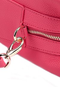 Angolo di una borsa a mano in pelle rosa con una cerniera e accessori in oro. Presenta una clip robusta e una superficie testurizzata.