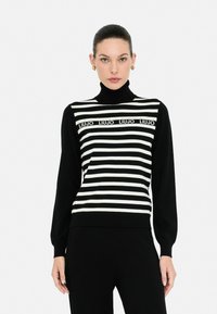Maglione a righe bianche e nere con collo alto, caratterizzato da una banda con logo sul petto e maniche lunghe, progettato con una silhouette aderente.