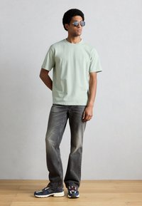 Mintovo zelené tričko s krátkym rukávom, sivé džínsové nohavice a viacfarebné tenisky. Okuliare s okrúhlymi sklami dotvárajú vzhľad. Jednoduchý, ležérny dizajn.