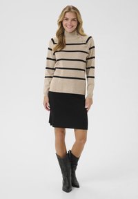 Beige gestreifter Pullover mit schwarzen Linien, hoher Kragen, seitlichen Knöpfen; kombiniert mit einem schwarzen knielangen Rock und schwarzen Cowboy-Stiefeln.