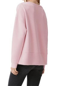 Jasnoróżowa bluza z luźnym krojem, okrągłym dekoltem i długimi rękawami. Wykonana z miękkiego materiału o lekko teksturowanym wykończeniu.