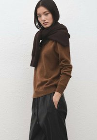 Brown wool sweater with a relaxed fit, paired with loose black trousers. A dark scarf is draped over the sweater's shoulders. Clean background.