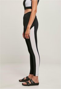 Fekete-fehér, magas derekú leggings, oldalsó színblokkal, sima textúrával és testhezálló fazonnal. Fekete szandállal viselve.