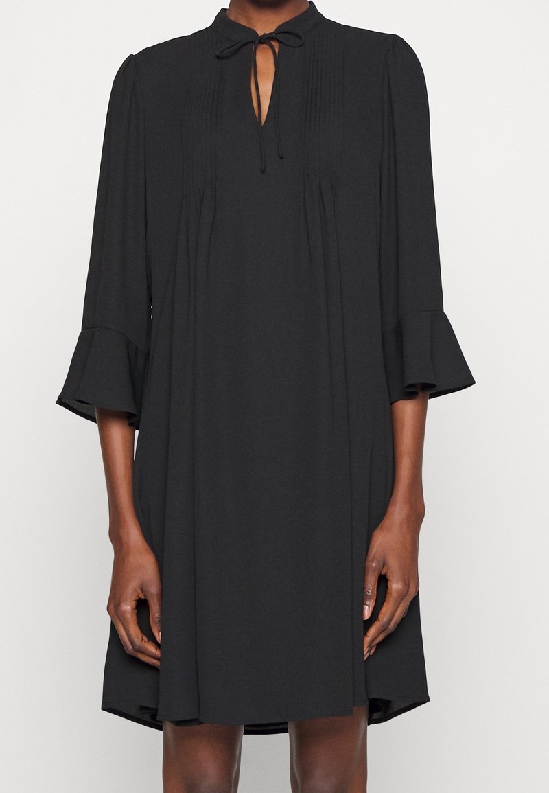 Robe noire avec un devant plissé, un détail de lien au col et des manches évasées trois quarts. Tissu doux, longueur au-dessus du genou, design minimaliste.