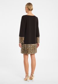 Schwarzes Kleid mit langen Ärmeln, verziert mit goldfarbenem Leopardenmuster und Stoff an den Manschetten und dem Saum. Glatte Textur mit geradem Schnitt.