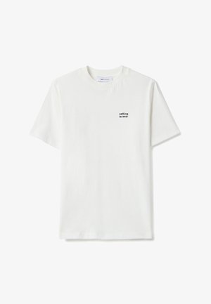 Weißes Baumwoll-T-Shirt mit kurzen Ärmeln und rundem Halsausschnitt, mit kleinem schwarzem Text „nothing to wear“ auf der linken Brustseite.