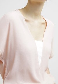 T-shirt rose clair à col en V avec des manches courtes, fabriqué en tissu doux et texturé. Présente une couche blanche visible au niveau de l'encolure.