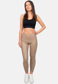 Top corto nero e leggings beige, realizzati in materiale elastico. I leggings hanno una texture liscia e una cintura alta. Sneakers bianche completano l'outfit.