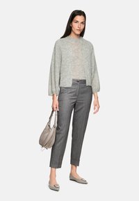 Light gray knit cardigan with balloon sleeves over a light beige top, paired with gray pinstripe trousers and pointed-toe flats. Holds a gray bag.