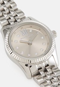 Sølv rustfritt stål klokke med rund kasse, en beige urskive, diamant time markører, og en ribbet bezel. Har en metall lenke armbånd.
