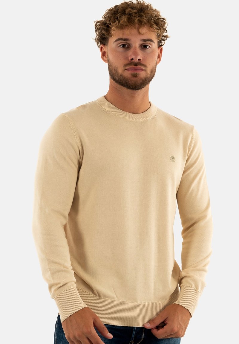 Maglione beige a maglia con colletto rotondo, polsini e orlo a coste, e un piccolo logo sul petto. Texture morbida e design aderente.