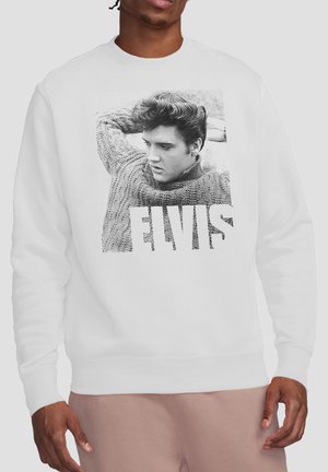 Mann trägt weißen Pullover mit schwarz-weißem Foto von Elvis Presley in einem Pullover und dem Text "ELVIS" unter dem Bild.