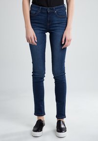 Jeans ajustados de mezclilla azul oscuro con ligero estiramiento, que cuentan con bolsillos frontales, cierre de cremallera y un acabado limpio en el tobillo.