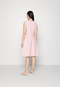 Vaaleanpunainen ruutukuosisinen mekko, jossa on liehukehame, hihaton muotoilu, tekstitetty kangas ja takana vetoketju. Yhdistetty valkoisiin remmisandaaleihin.