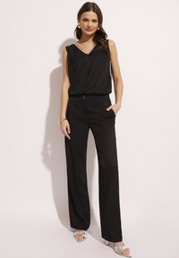 Czarny bezrękawnik z dekoltem w serek i białym wykończeniem, zestawiony z czarnymi spodniami o wysokim stanie z bocznymi kieszeniami i dopasowanym krojem.