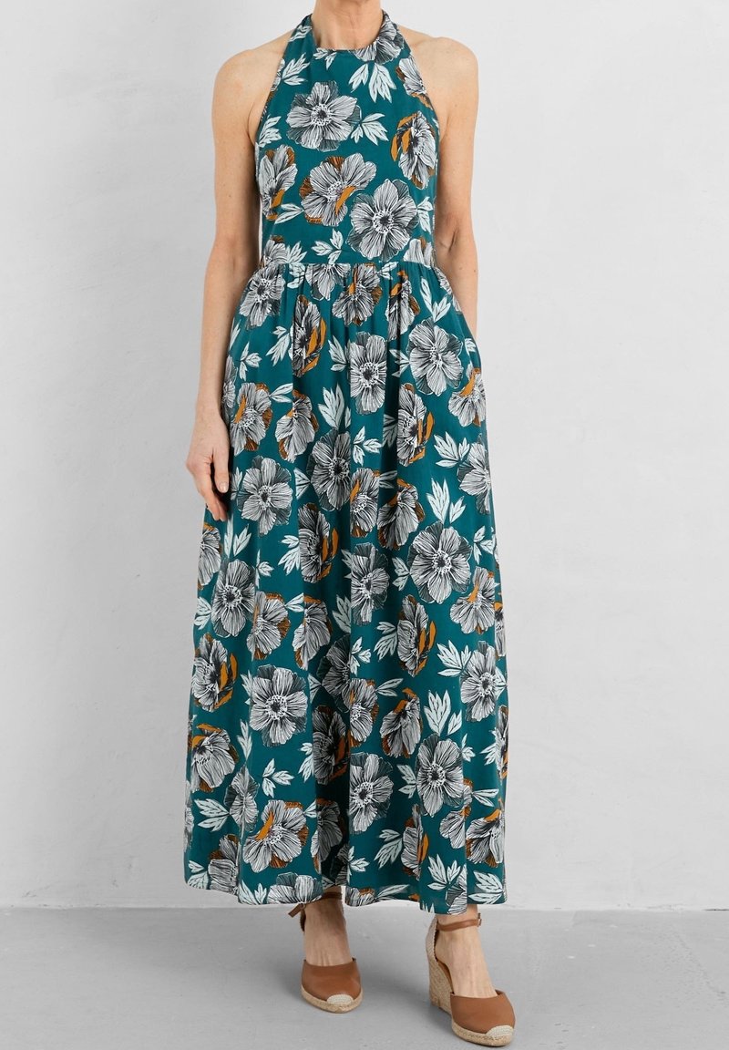 Robe maxi florale en tissu teal avec des fleurs noires et blanches agrémentées d'accents orange, décolleté halter, corsage ajusté et jupe fluide.