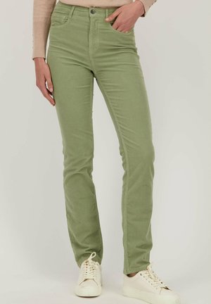 Pantalons en coton slim fit verts avec poches avant, fermeture à bouton et détails de couture subtils, associés à des baskets blanches.