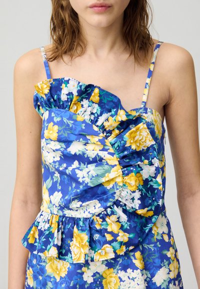 Robe florale bleue, ornée de fleurs jaunes et blanches, avec un col froncé et un ourlet en peplum. Fabriquée en tissu léger avec des bretelles ajustables.