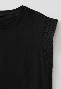 Haut noir à manches courtes avec encolure ronde et détail décoratif en dentelle ajourée florale sur les manches.