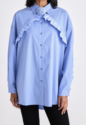 Chemise à rayures bleu clair et blanche avec des détails froncés et un accent floral au col, dotée de manches longues et d'une coupe décontractée.