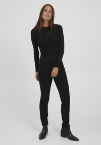 Zwarte top met lange mouwen en een gegolfde onderrand, gecombineerd met zwarte aansluitende broek en enkellaarsjes. Glad textuur en minimalistisch ontwerp.