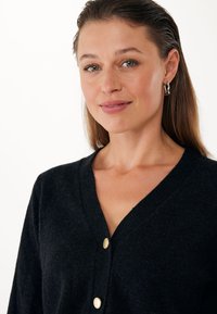 Cardigan in lana nera con scollatura a V, tre bottoni dorati frontali e una finitura morbida e testurizzata.