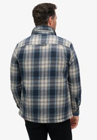 Camicia di flanella in blu, blu navy e crema con motivo a quadri. Maniche lunghe con polsini abbottonati, colletto e orlo dritto. Texture morbida.